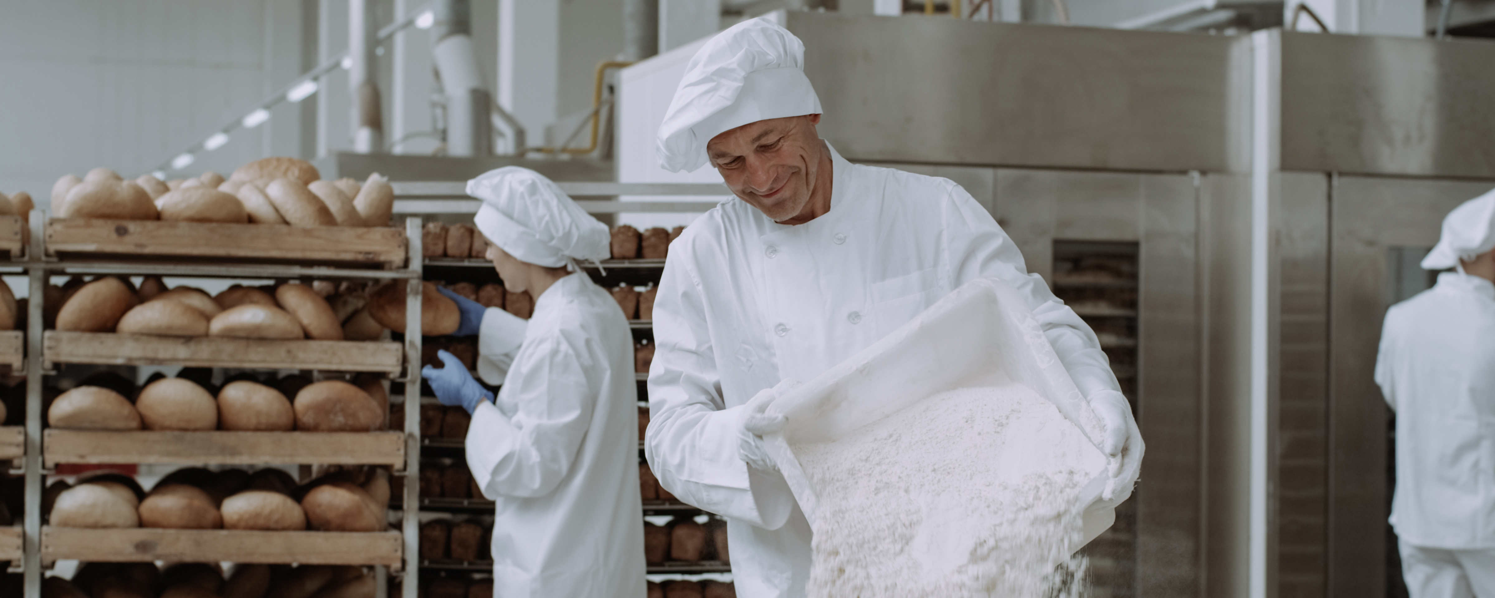 A baker adds flour to a mixing drum.