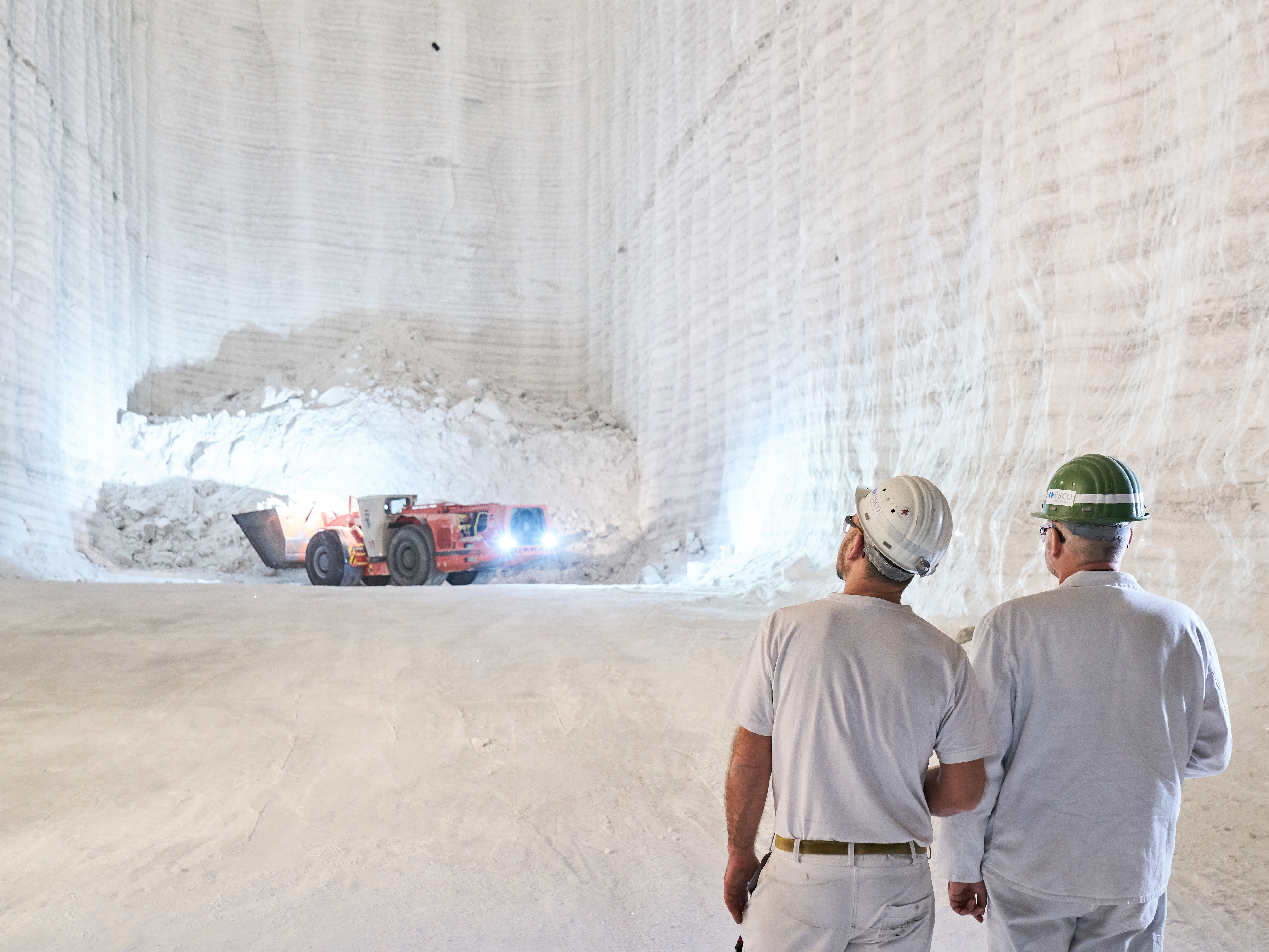 Underground, red wheel loader with shovel, two employees in PPE